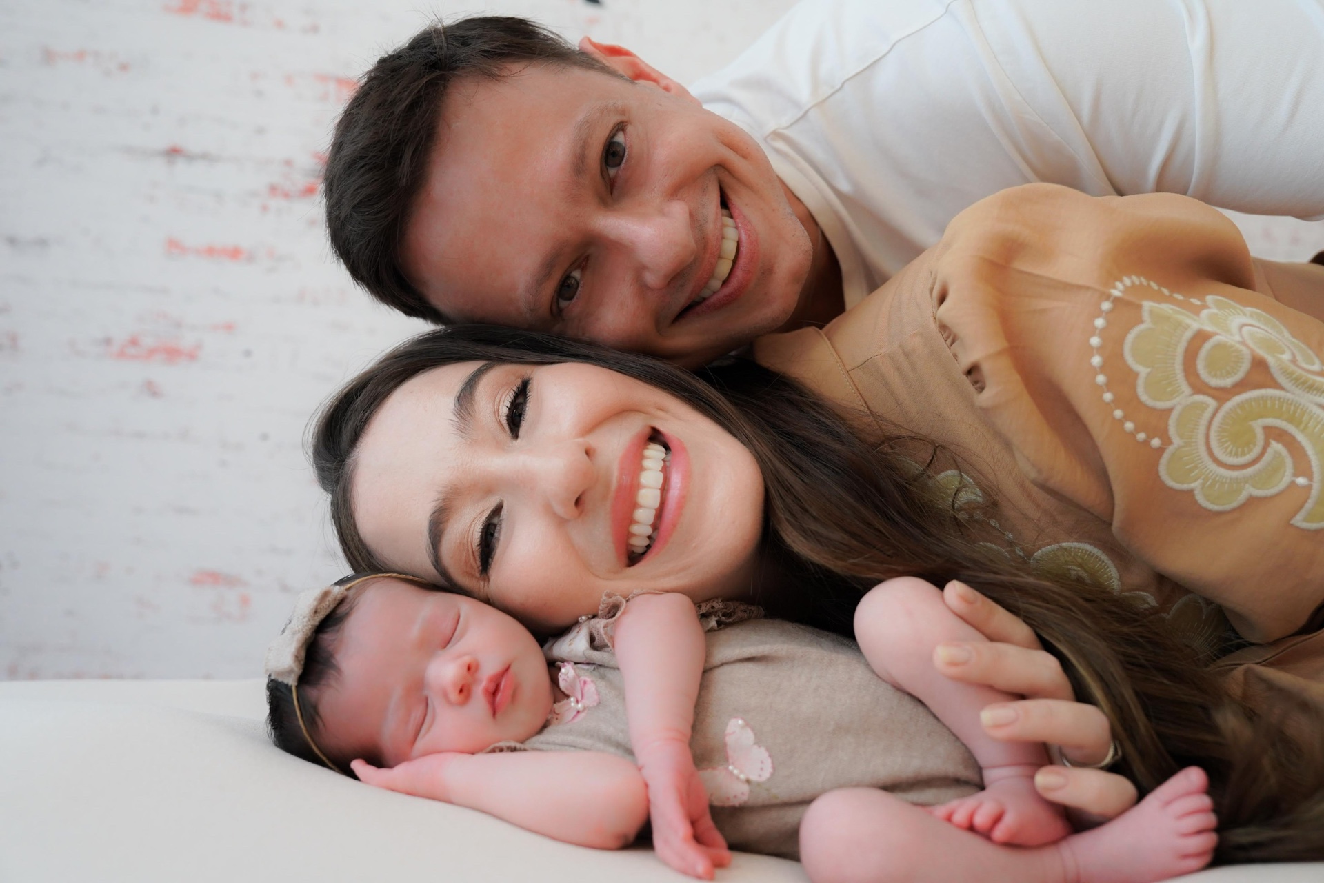Gabriela e Marcelo sorrindo abraçados com a recém-nascida Sofia