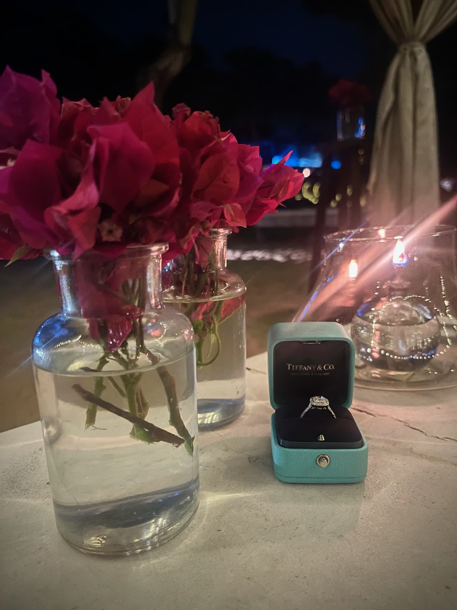 Anel de noivado em uma caixinha Tiffany ao lado de rosas vermelhas e velas